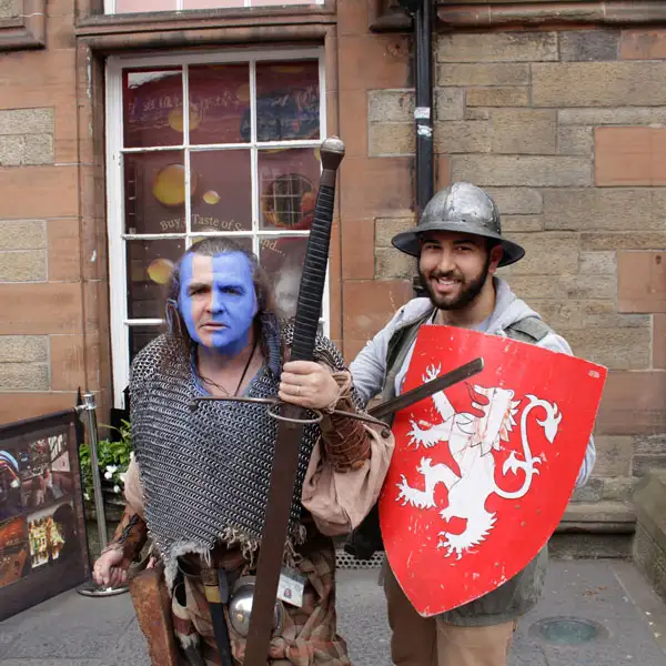 A student holding a shield and smiling next to a Scandinavian actor wearing face paint