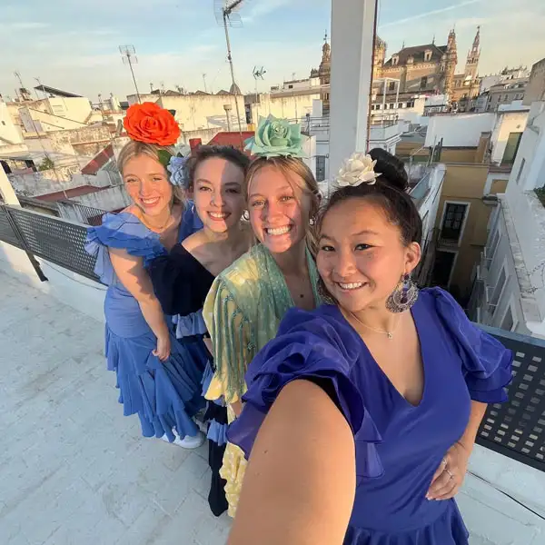 4 students standing up high in a city wearing dresses and taking a selfie