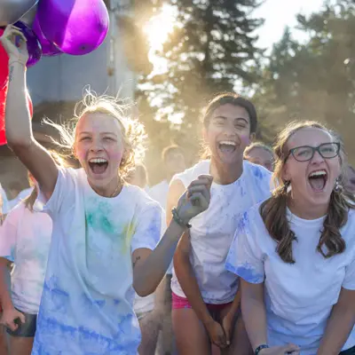 Three students smile and chear excitedly in the sunshine for the Color Run