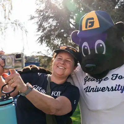 A George Fox alumna taking a selfie with mascot Pennington