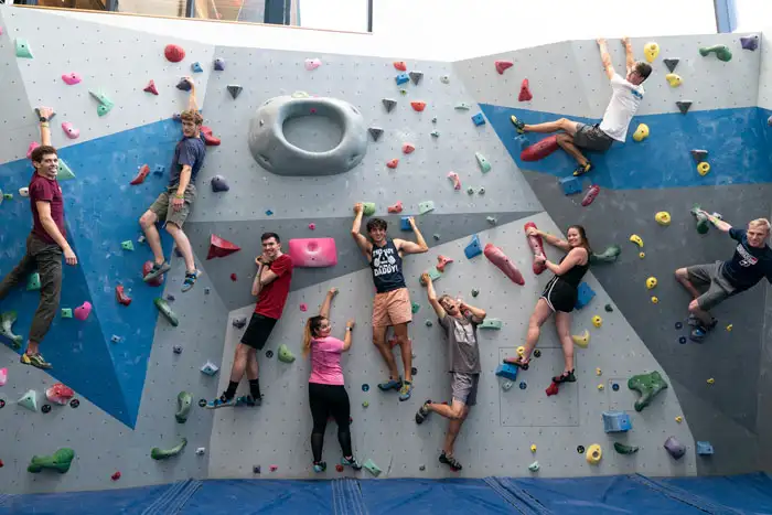 A group of students hanging on the George Fox rock wall and looking at the camera