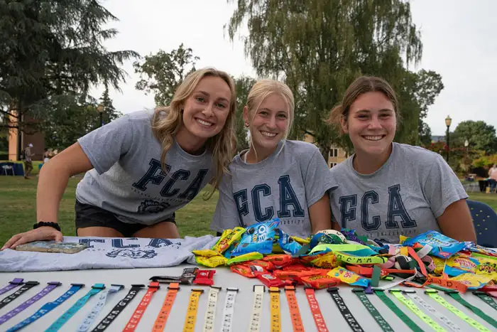 3 students wearing Fellowship of Christian Athletes t-shirts at their club table