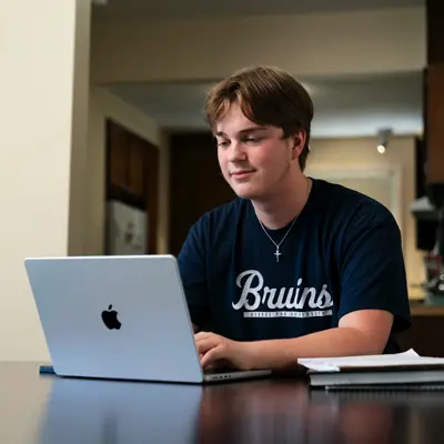 Student sitting at a kitchen table doing school work on his laptop