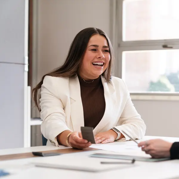 A student laughing while she explains something on a table while wearing professional attire