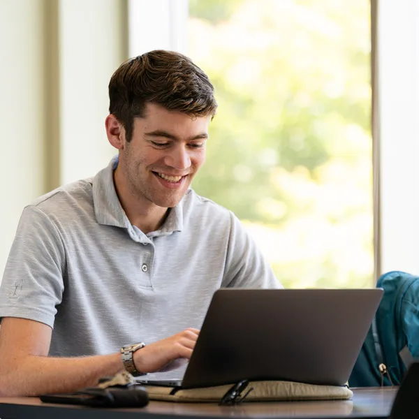 Online student works on a laptop and smiles