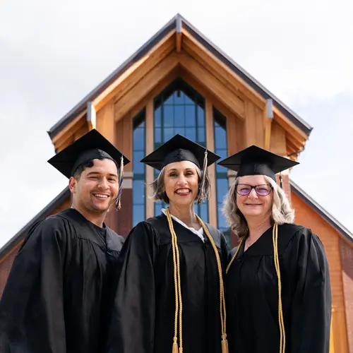 Three adult graduates smiling together in their caps and gowns