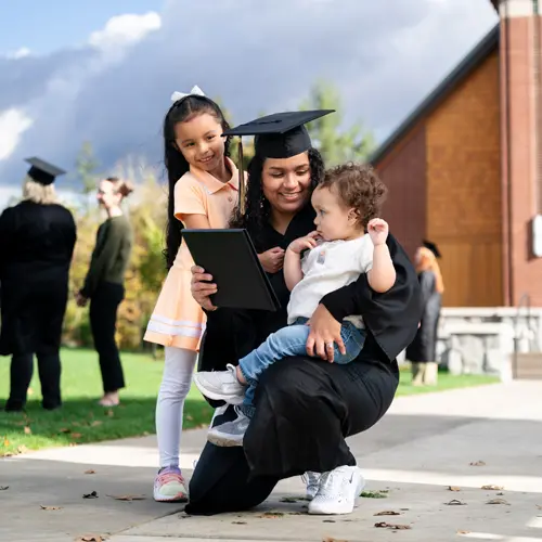 Woman celebrating graduation in her cap and gown with two children