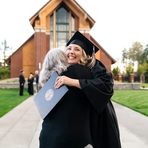 Graduate hugging someone tightly with a big smile on her face and a degree in her hand