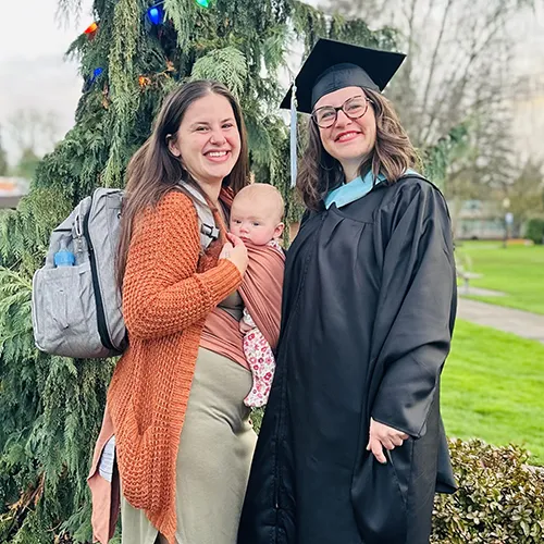 Sara Noelle Goodman in graduation robe in front of a Christmas tree