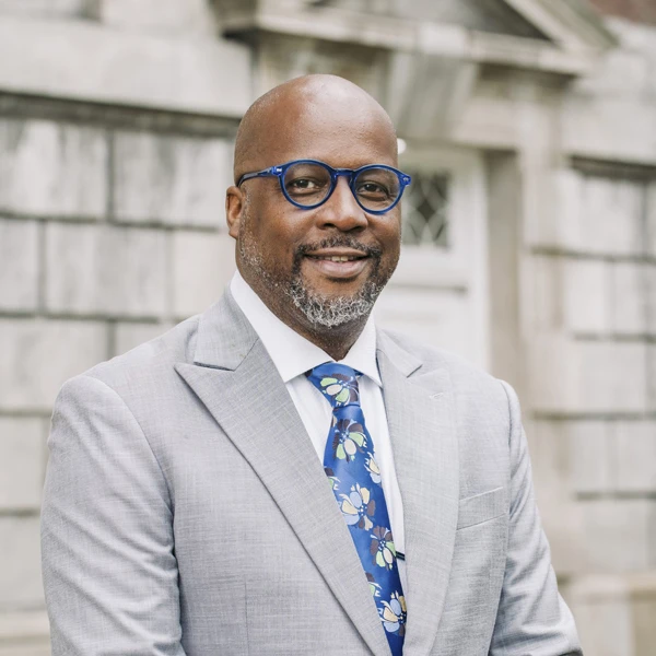 Daren Jaime smiling in a grey suit with blue glasses and a blue tie