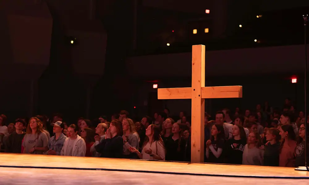 Photo of a cross and students worshiping in the background