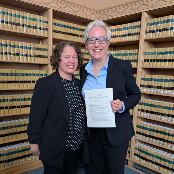 Lisa Jones and Tina Kotek smile and hold a document in the Oregon State Building