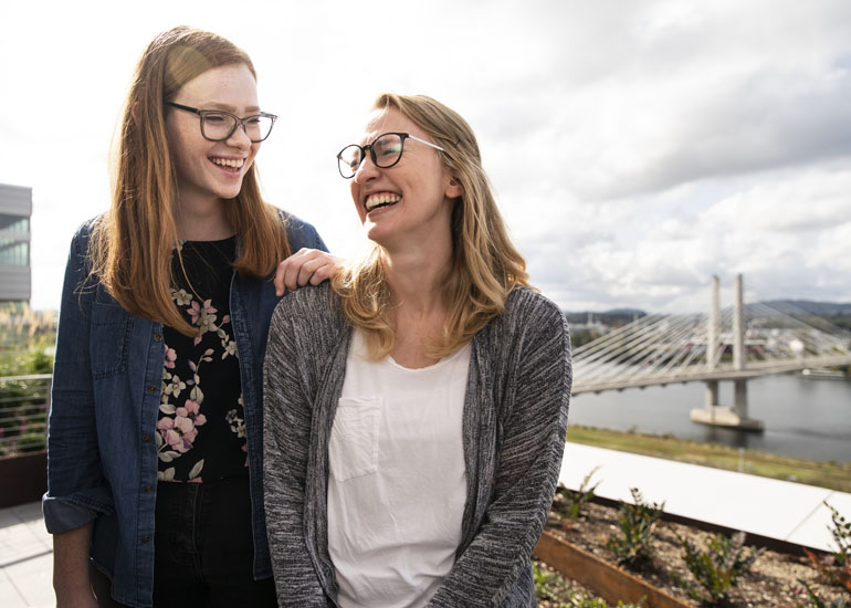 Photo of Quinlan Morrow and Brittany Smith laughing besides a bridge in Portland, OR