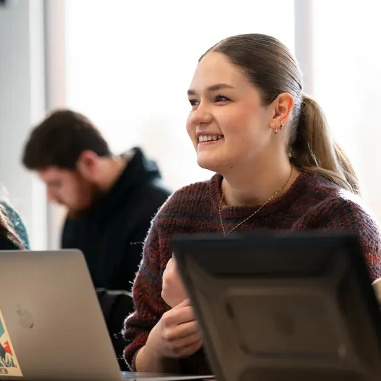 Two students in a classroom together. One student is engaged and smiling while the other student is focused on their work.