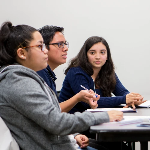 Three students sitting at a desk having a discussion