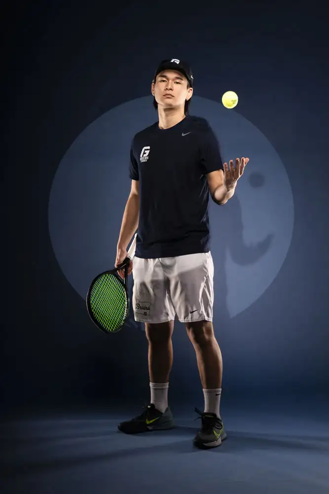 George Fox tennis athlete throwing a ball in the air while looking at the camera