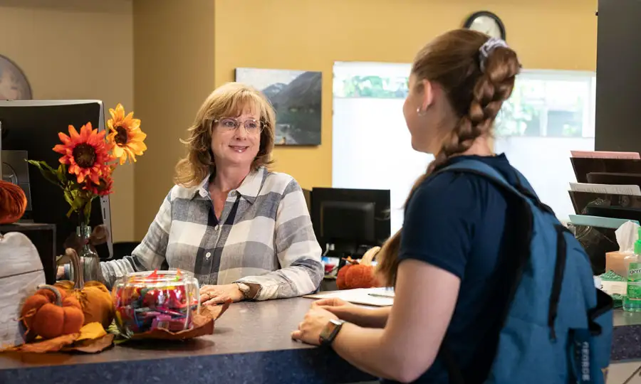 A woman helping a student at the front desk of the Health & Counseling Center