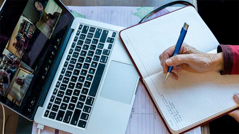 Staff member writes on a notebook while on a Zoom meeting