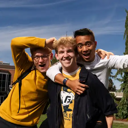 Three students messing around smiling at the camera in George Fox gear