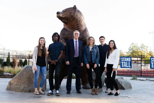Students standing around Robin Baker in front of Mama Bear