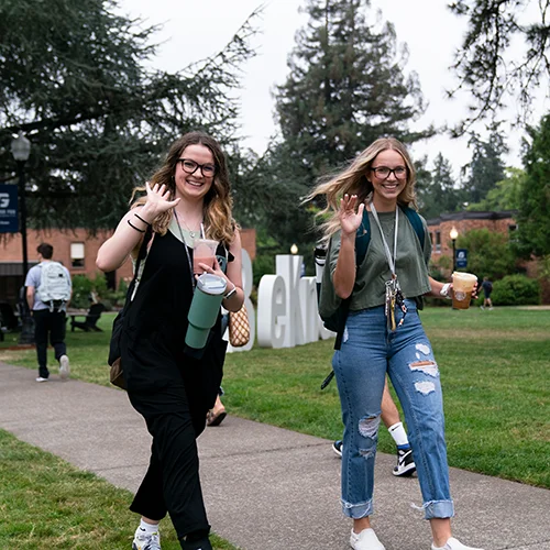 Two women visiting campus waving at the camera