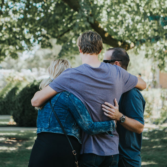 Family stands outside on a sunny day, embracing each other. Notably, not a stock photo.