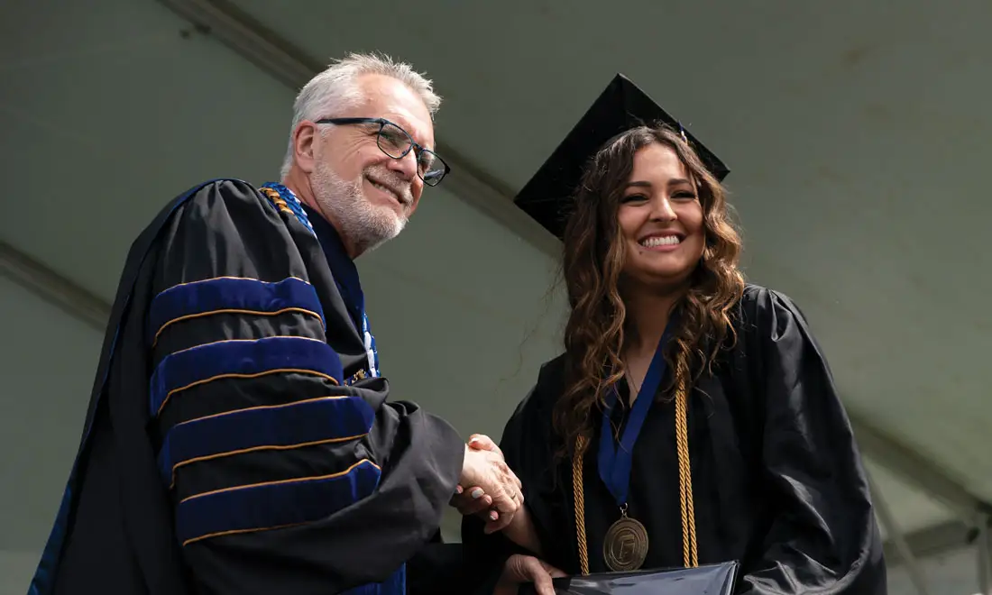 Robin Baker shakes a student's hand at graduation