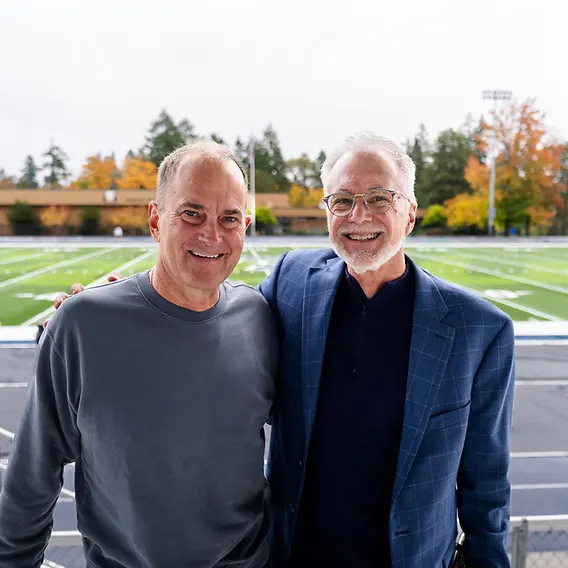 Robin Baker stands for a picture with Tim Davis in front of the football field