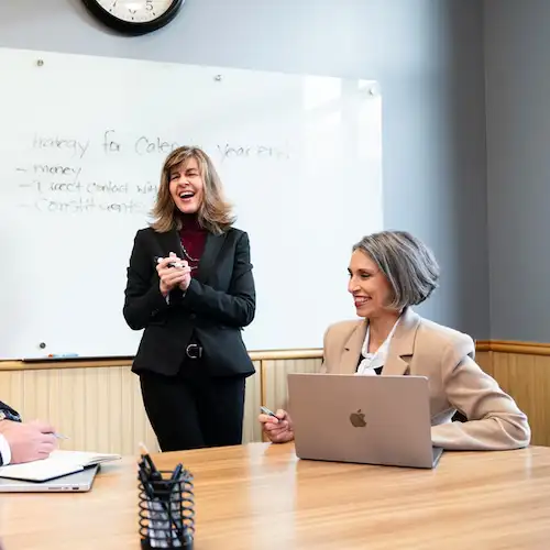 Two professional women meeting and laughing in front of a white board