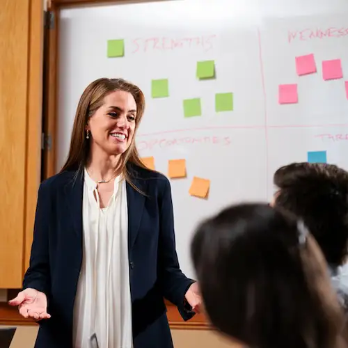 Professional smiling speaking to colleagues in front of a white board with sticky notes