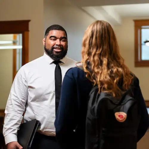Education professional smiling speaking with a student in a hallway