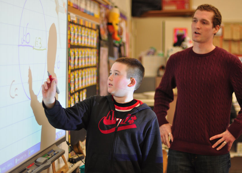 Student teacher assists student use a smartboard