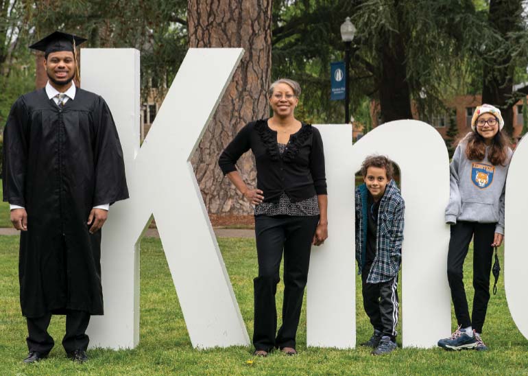 A student and family pose by the large 'Be Known' letters on campus