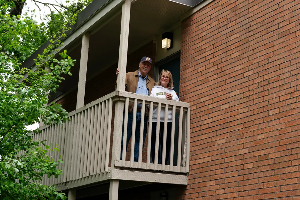 Dave and Debbie Powell smiling together in George Fox gear atop the stairway of Weesner Village Apartments