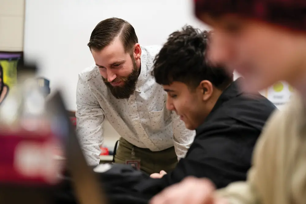 Roy working with a student in the classroom with a gentle smile of satisfaction
