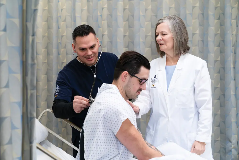 Loretta Krautscheid observes as Sanchez examines a patient in the George Fox nursing skills lab