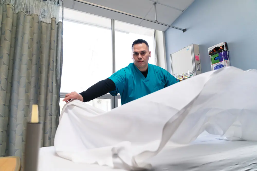 Sanchez in scrubs placing a white sheet on a bed in the medical-surgical ward at Kaiser Permanente in Beaverton, Oregon.