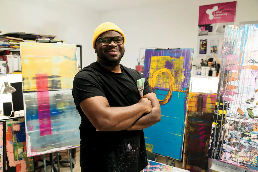 Eans smiling proudly in front of his artwork with his arms crossed