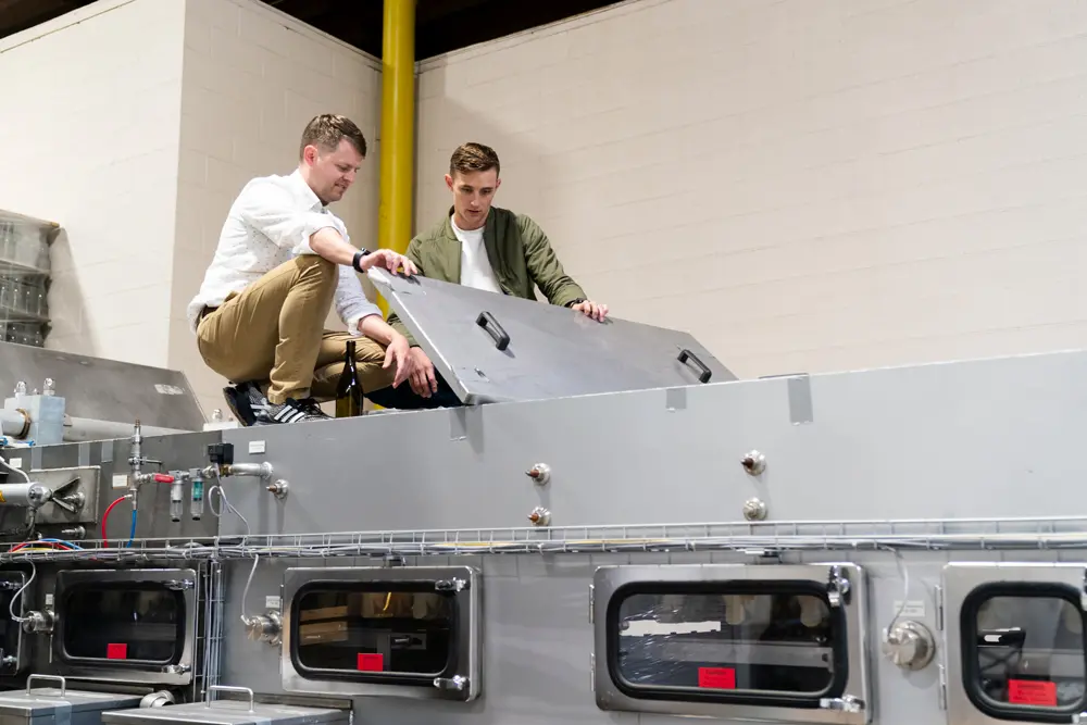 O’Hern and business partner Adam Rack atop and looking inside their custom bottle washing machine