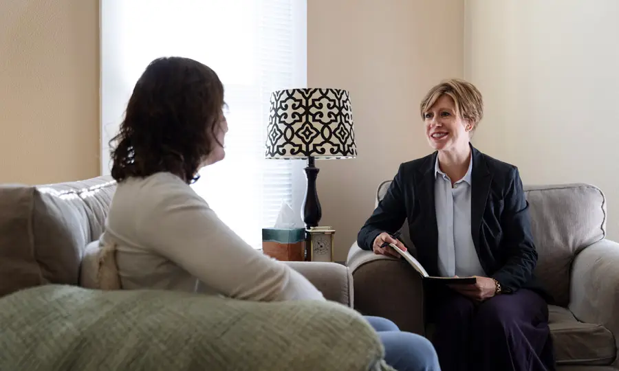 Female mental health professional talks with a patient in a beige, soft lit room