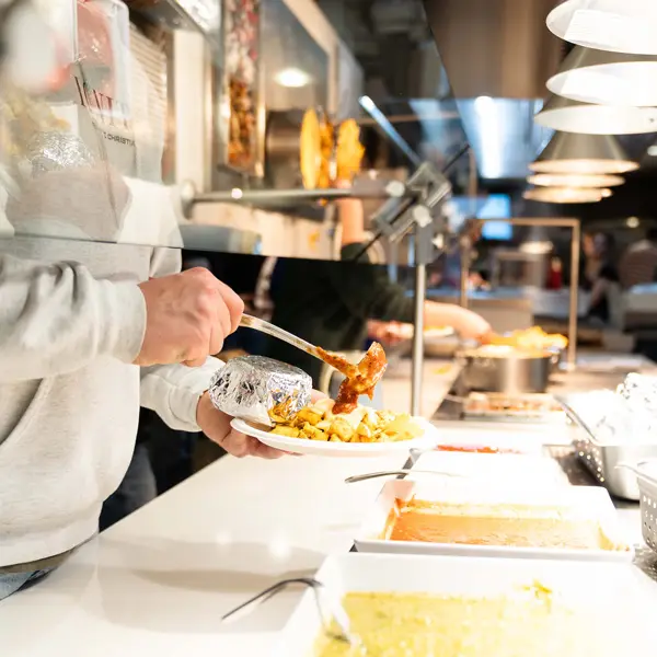 a student scoops pasta sauce onto their dish