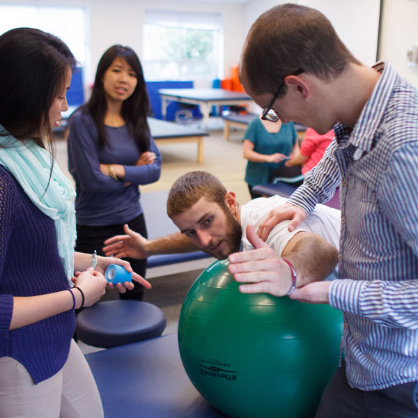 3 students help a guy on an exercise ball