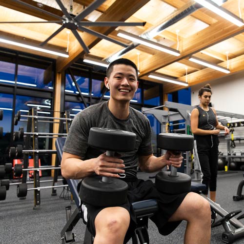 student poses with dumbbells in the gym 