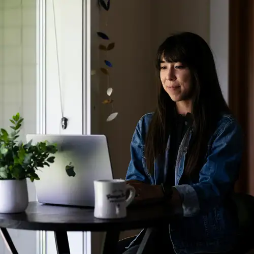 Student works on her computer in a cozy setting with a coffee mug