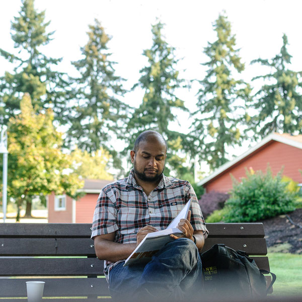 student reads a book on a bench outside