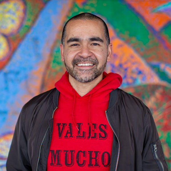 Joel in a red sweatshirt standing in front of a mural